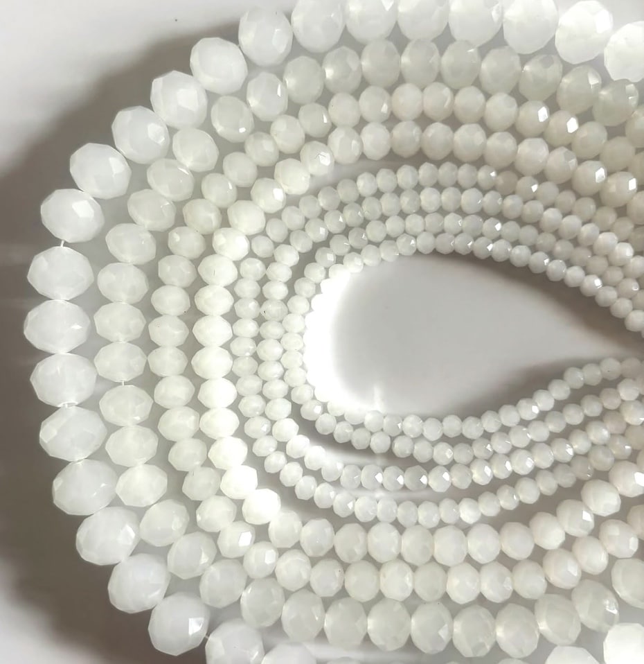 Close-up of several strands of round, faceted white beads arranged in concentric circles on a white surface, resembling the elegant patterns you might create for beaded garden stakes DIY projects.